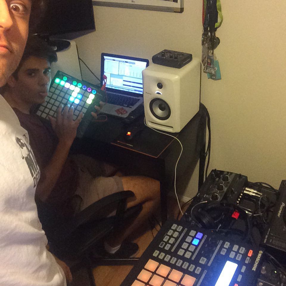 Two young producers pulling faces at the camera over a Launchpad in a cramped bedroom studio